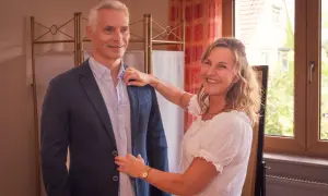 Frau hilft Mann beim Anprobieren eines Sakkos. Sie lächelt und richtet den Kragen. Welcher Style passt zu mir?