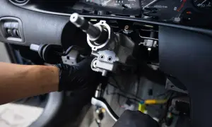 Mechanik w czarnej rękawiczce dokręca śrubę kluczem nasadowym przy kolumnie kierownicy.