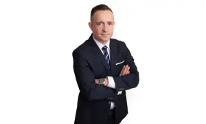 Mężczyzna w garniturze ze skrzyżowanymi rękami, na białym tle.
