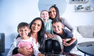Familjen njuter av sitt hem efter en lyckad svensk villarenovering. Två mammor och tre barn ler glatt mot kameran.