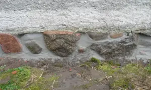 Das Feldsteinfundament wird mit Mörtel abgedichtet. Große Steine sind sichtbar, umgeben von frischem Mörtel, der die Lücken füllt.