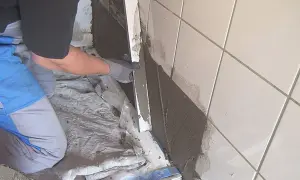 Hand trägt Abdichtung auf alten Fliesen auf.