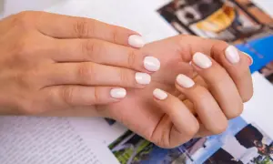 Delikatne, modne paznokcie french w odcieniu nude. Dłonie spoczywają na magazynie z kolorowymi zdjęciami.