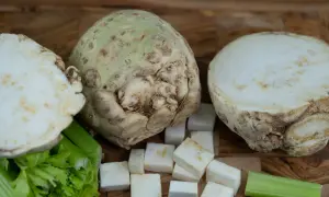 Knollensellerie-Rezepte für eine herzhafte Hauptspeise: Ein ganzer Knollensellerie, halbiert und gewürfelt, mit Staudensellerie auf Holzuntergrund.