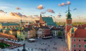 Zachód słońca nad Zamkiem Królewskim i Rynkiem Starego Miasta w Warszawie. Kolorowe kamienice, wieża zegarowa i chmury na niebie tworzą malowniczy widok.