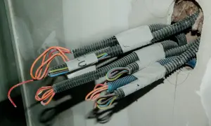 Przewody elektryczne w peszlach wychodzące ze ściany. Widać kolorowe żyły, gotowe do połączenia. To etap prac, jak przedłużyć przewód elektryczny w ścianie.