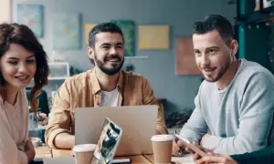 En grupp unga, leende människor diskuterar vid ett bord. En laptop och kaffekoppar antyder ett möte om utbildning, organisation och ledarskap.