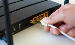 Dłoń podłącza kabel sieciowy do routera, przygotowując go do zmiany.