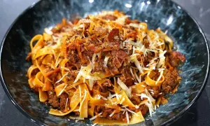 En skål med breda bandnudlar täckta av en mustig köttfärssås, toppad med riven ost och peppar. En härlig pasta ragu!