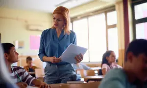 Nauczycielka z dokumentami w ręku, skupiona na uczniu. Jej zaangażowanie to klucz do awansu zawodowego nauczyciela.
