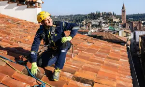 Operaio in corda per la riparazione tetto casa, con vista panoramica sulla città.