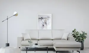 Divano angolare color crema, con tavolino rotondo in vetro, pouf bianco e quadro astratto. Le misure divano angolare sono perfette per questo spazio.
