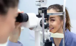 Kobieta uśmiecha się podczas badania wzroku u okulisty za pomocą specjalistycznego sprzętu.
