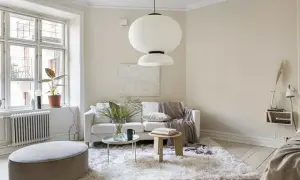 Ljust vardagsrum med en vit soffa, fluffig matta och en stor taklampa. Naturinredning med växter och trädetaljer skapar en lugn atmosfär.