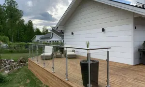 Träaltan med glasräcke och utemöbler. Huset är målat vitt, och det ser ut som att det nyligen har fått en ny omgång med olja på staketet.