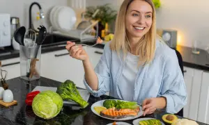 Femme souriante dégustant un menu équilibré pour perdre du poids : saumon, brocolis, avocat, noix et légumes frais.