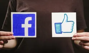 Dwie ręce trzymają kartki z logo Facebooka i kciukiem w górę.