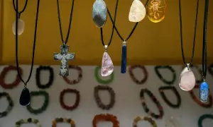 Wisiorki z kamieni, w tym krzyż z rybami, symbol siły kobiecej, i bursztyn ze skorpionem, wiszą na tle bransoletek.