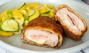 Zwei goldbraune Cordon Bleu, gefüllt mit Schinken und Käse, daneben ein bunter Kartoffel-Zucchini-Salat. Ein leckeres Cordon Bleu Rezept!