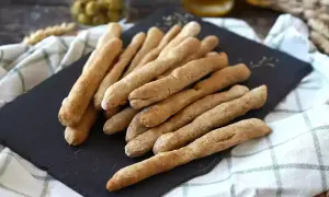 Une pile de gressins dorés, parfaits pour une recette gressin maison. Des olives et une boisson en arrière-plan.