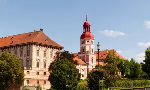 Schloss Roudnice nad Labem mit seinem roten Turm und den Ziegeldächern, umgeben von grünen Bäumen.