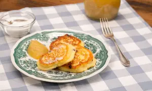 Quarkkeulchen ohne Kartoffeln, goldbraun gebacken, mit Apfelmus und Zucker bestreut, auf einem Teller mit grünem Muster.