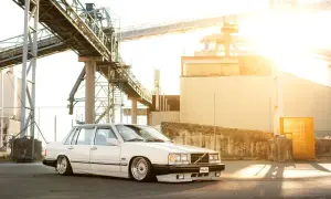 Vit Volvo 740 från 1990, sänkt och med kromade fälgar, parkerad vid en industrianläggning i solnedgången.