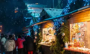 Mercatini di Natale nelle Marche: bancarelle illuminate da lucine blu, neve che cade e gente che passeggia tra gli stand.