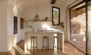 Cocina luminosa con isla central, taburetes y vistas a un patio de piedra, ideal para casas de campo modernas.