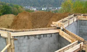 Fundament budowlany z szalunkiem i zbrojeniem, w tle domy i las.