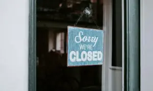 En blå skylt med texten "Sorry WE'RE CLOSED" hänger i ett fönster. Enskild firma i vilande.