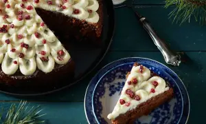 En mjuk pepparkaka med frostning och röda bär. En bit är upplagd på en blåvit tallrik, redo att avnjutas.