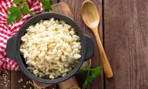 Kasza bulgur w czarnej misce, obok drewniana łyżka i natka pietruszki. Niska kasza bulgur indeks glikemiczny.