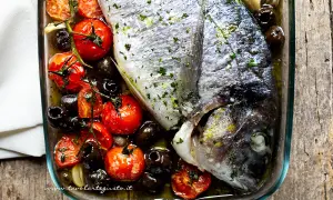 Orata al forno con pomodorini, olive nere e aglio, un piatto semplice e gustoso pronto per essere infornato.