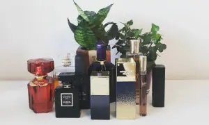 Kolekcja perfum: czerwony Chopard, czarny Coco Noir Chanel 100ml, fioletowy i złoty Michael Kors, oraz inne, otoczone zielenią.