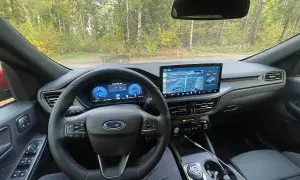 Wnętrze Ford Kuga z nowoczesnym ekranem multimedialnym i cyfrowymi zegarami. Kierownica z czerwonymi przeszyciami i przyciskami.