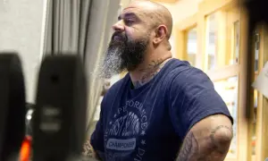 Man med skägg och tatueringar, klädd i en t-shirt med texten "Performance First Session Championship". Kanske en del av "kaka kartellen" som förbereder sig för något.
