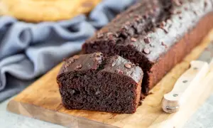 Fetta di banana al cioccolato, soffice e ricca, con gocce di cioccolato fondente, su tagliere di legno.