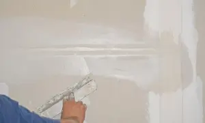Hand spachtelt eine Rigips-Wand glatt. Die Naht wird mit Spachtelmasse bedeckt, um eine ebene Oberfläche für die weitere Bearbeitung zu schaffen.