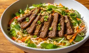 En skål med asiatisk biffsallad med tunna nudlar, strimlad biff, gurka, morötter, mynta och jordnötter.