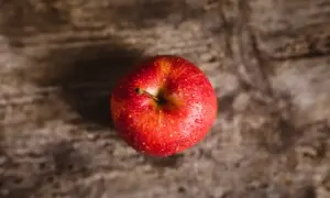 Czerwone, lśniące jabłko z kroplami wody na drewnianym tle. Niskie jabłko indeks glikemiczny to zdrowa przekąska.