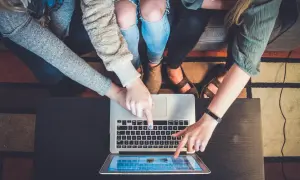 Flera personer pekar på en laptop och en surfplatta, ett tydligt exempel på delaktighet i ett projekt.