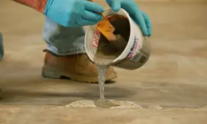 Man con guantes azules vierte mortero para reparación de fisuras en soleras de hormigón.