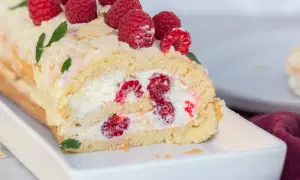 Himbeer Biskuitrolle mit frischen Beeren und Sahne gefüllt, dekoriert mit Mandelsplittern und Minze. Ein Genuss!