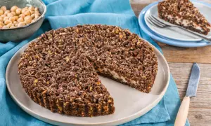 Sbriciolata ricotta e cioccolato con croccante copertura di nocciole e cacao. Una fetta è già servita su un piattino.