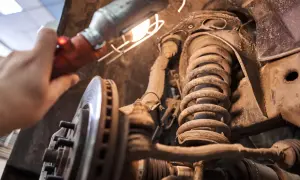 Une main éclaire avec une lampe un amortisseur qui grince, une pièce rouillée et poussiéreuse du système de suspension d'une voiture.