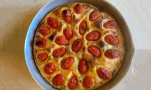 Focaccia foggiana dorata e fragrante, con pomodorini succosi e erbe aromatiche, pronta per essere gustata.