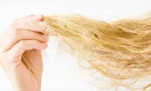 Dłoń trzyma pasmo blond włosów, które wyglądają na zniszczone i suche.