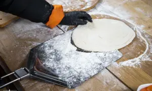 Hand mit Handschuh legt Teig auf bemehltes Pizzaschaufel.