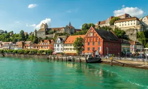 Meersburg Tourismus: malerische Altstadt mit bunten Häusern und Burg am Hang, überragt von grünen Hügeln, am glitzernden Bodensee.
